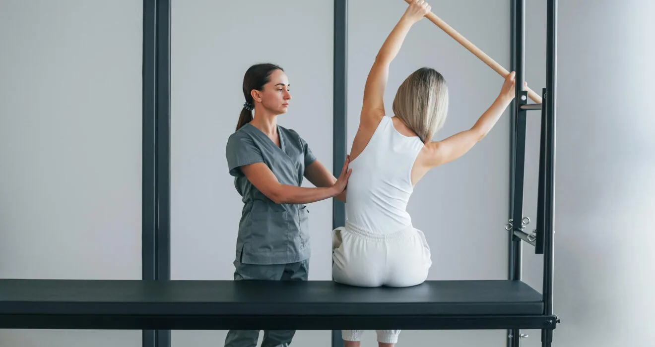 Fizyoterapist eşliğinde pilates yapan kadın.